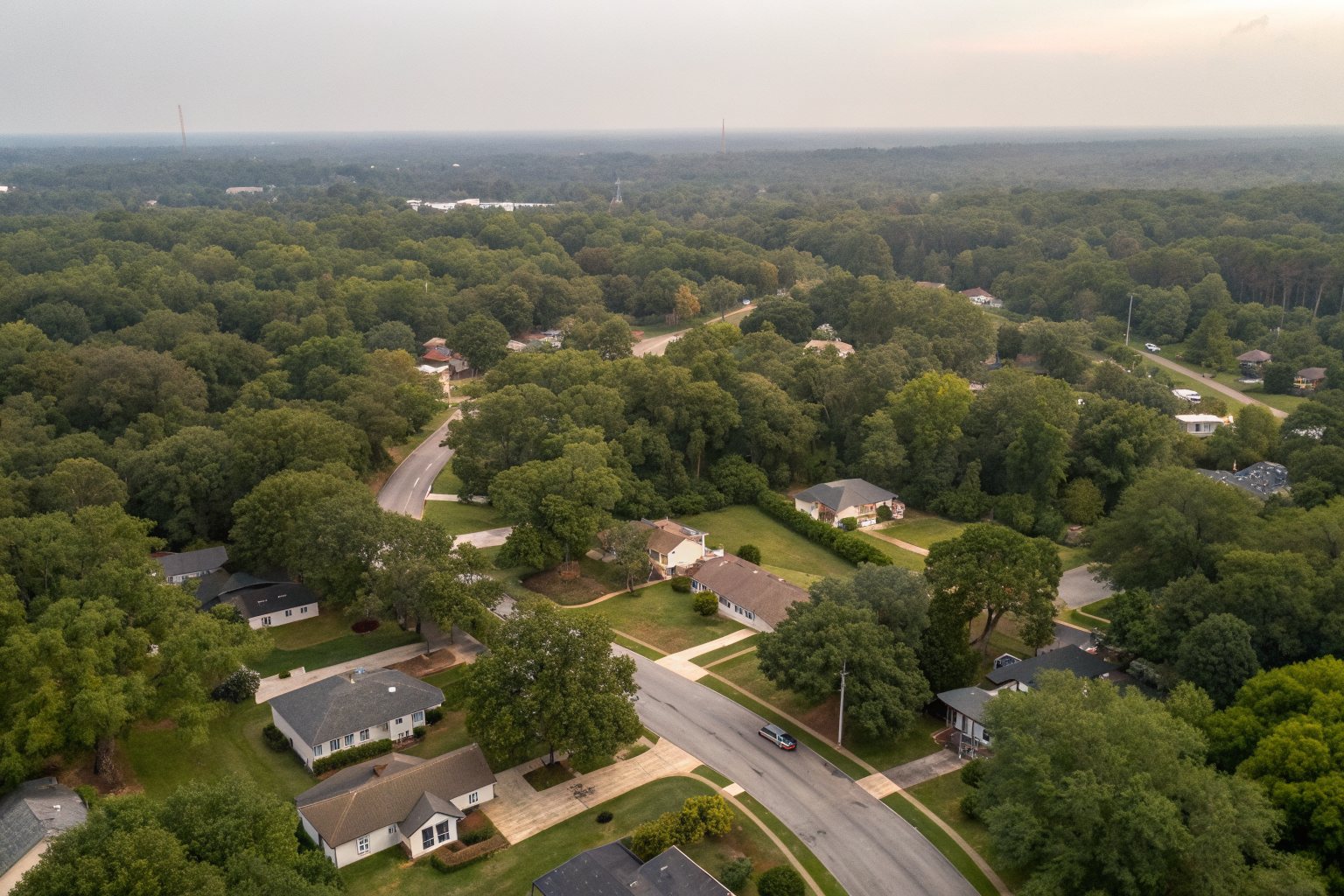 Aerial view of ranch-house roofs among oaks and pines along curving neighborhood streets